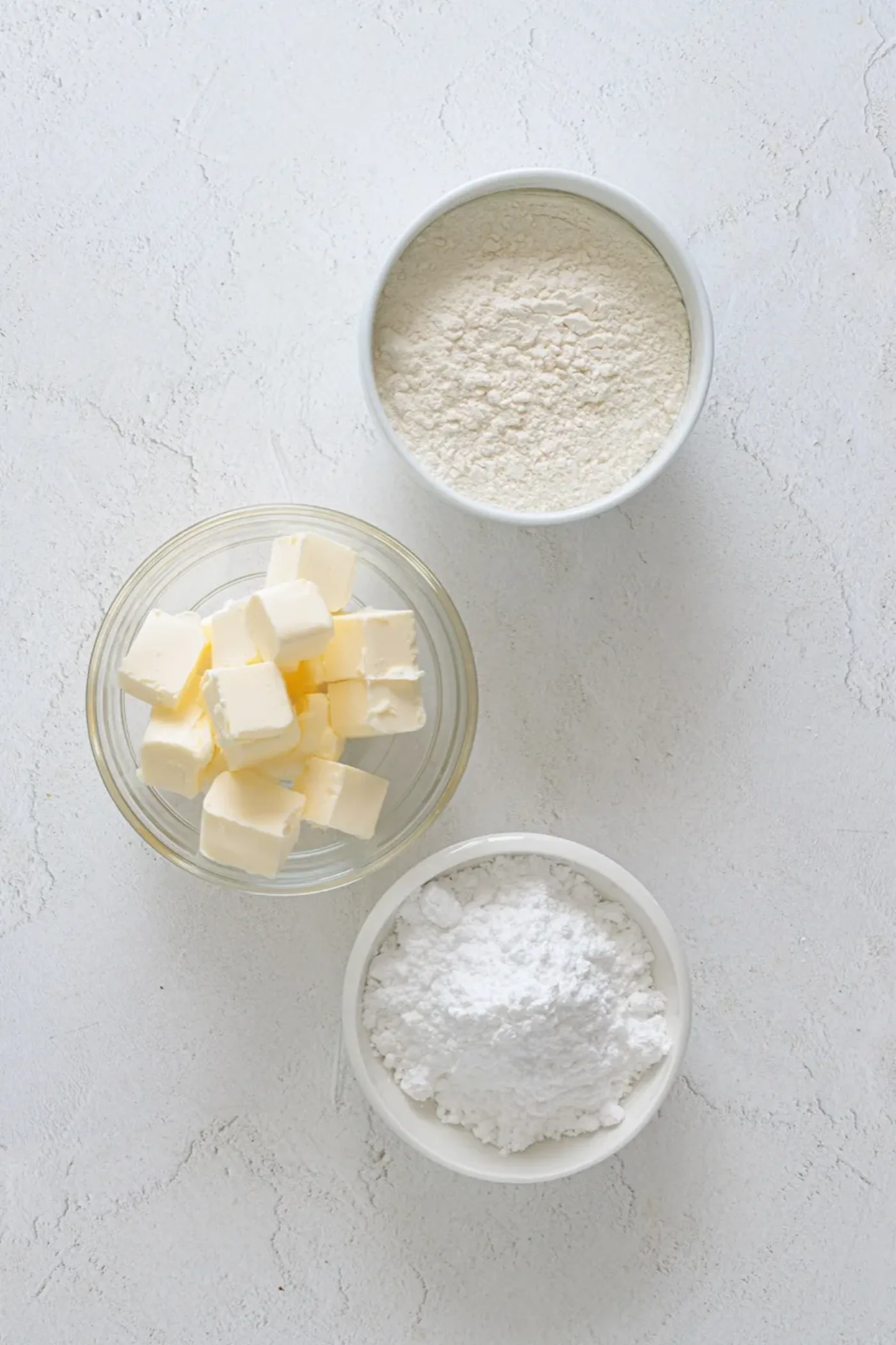 Bowls of butter, powdered sugar, and all-purpose flour measured for butter cookies