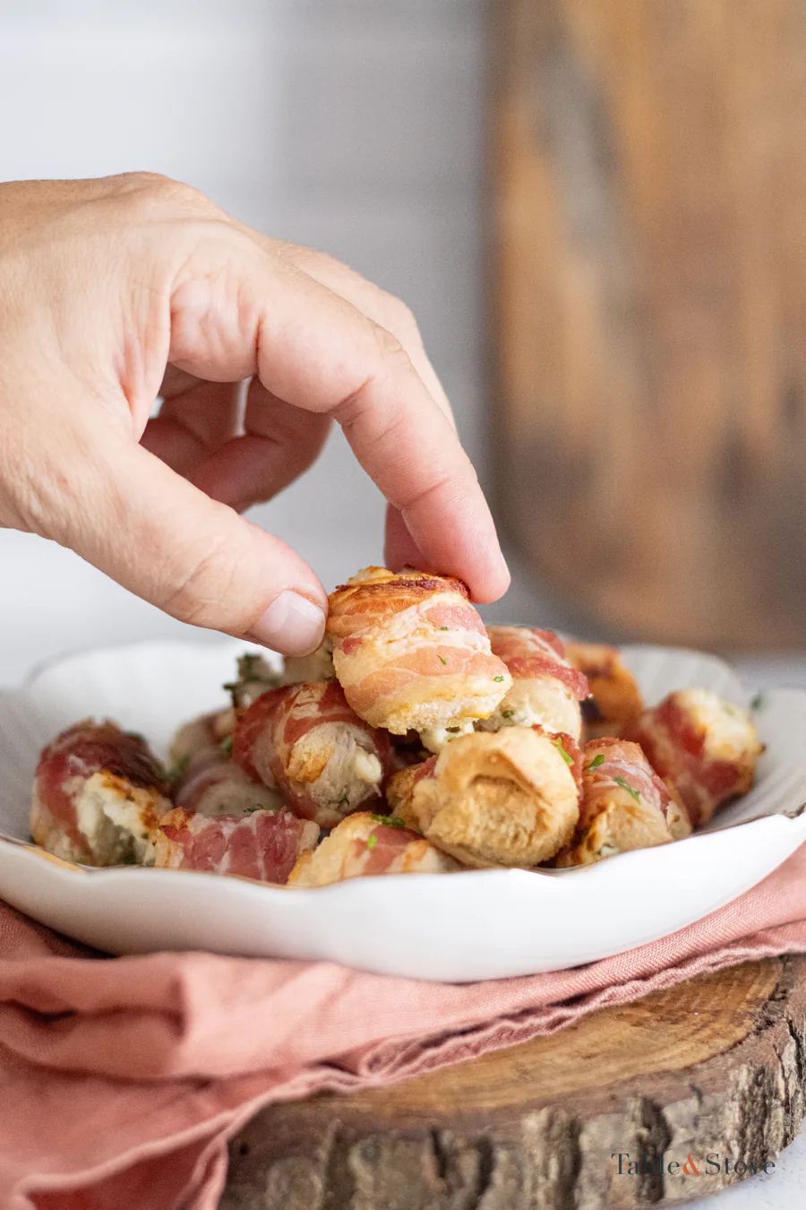 Hand lifting one bacon cheese bite from a serving bowl