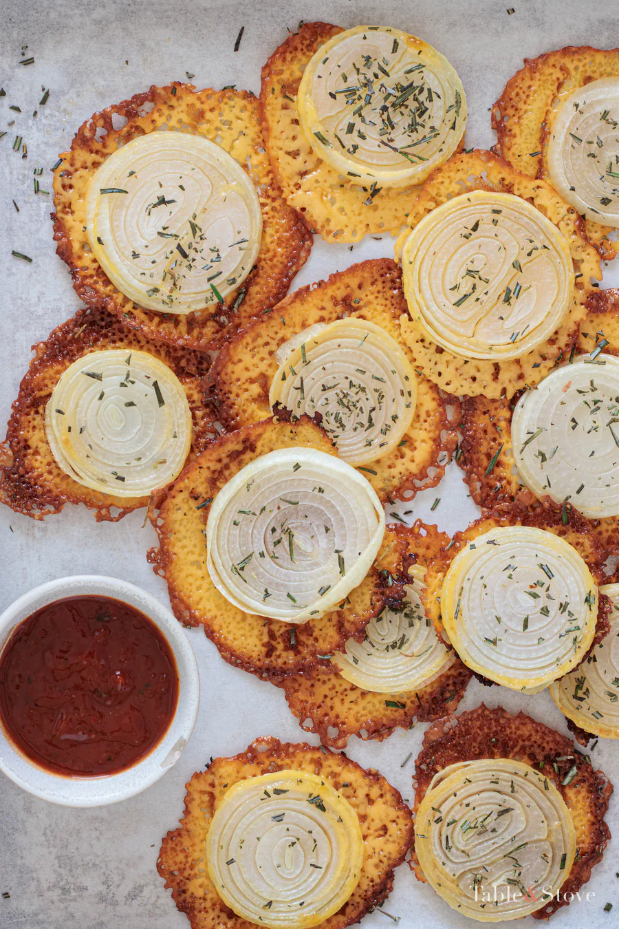 Cheesy onion crisps spread across a board beside dipping sauce