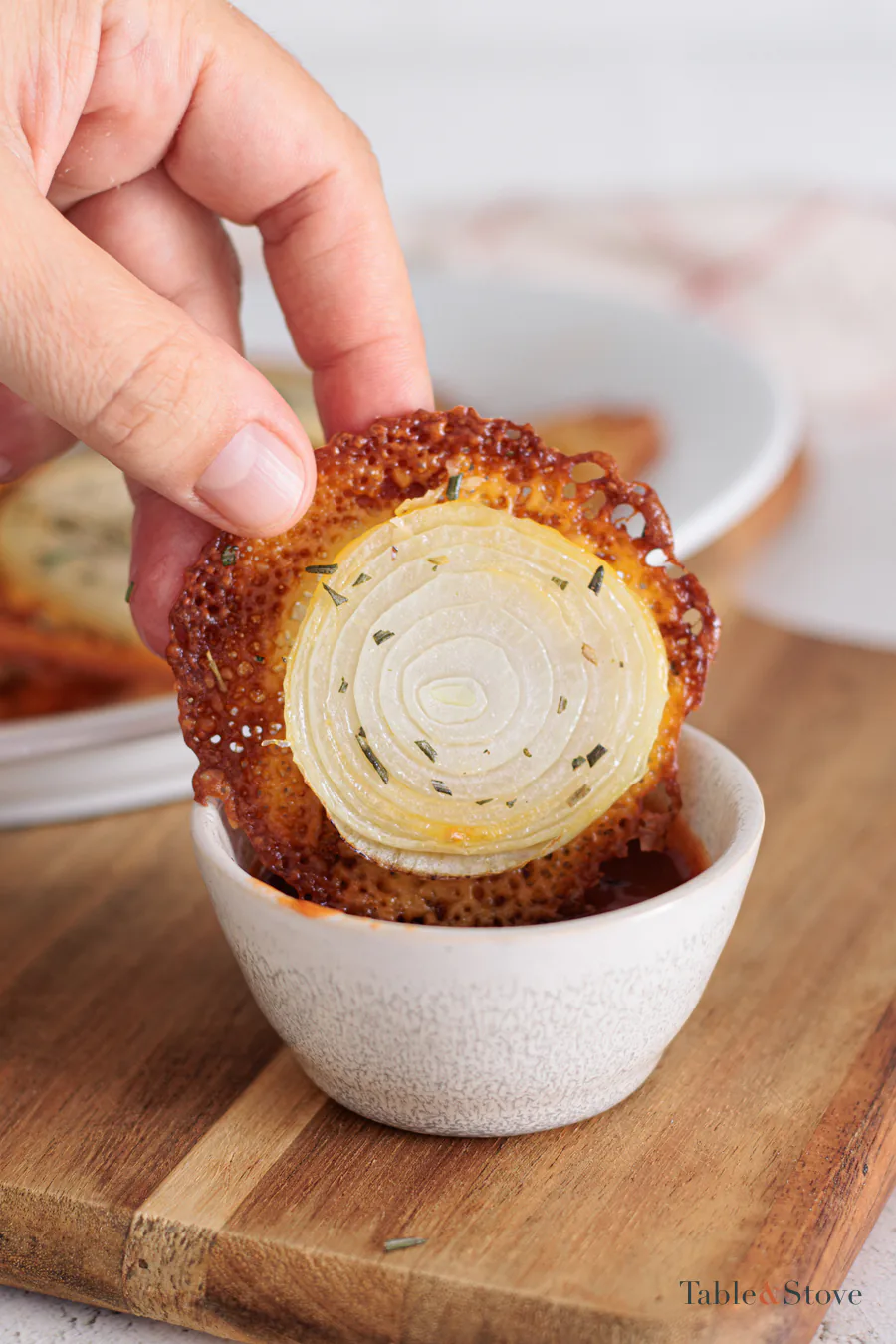 Hand dipping one cheesy onion crisp into sauce