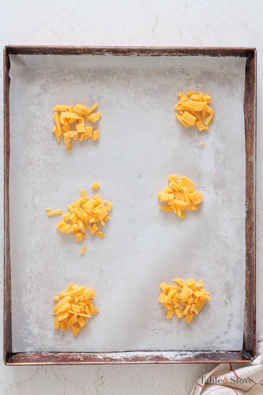 Small piles of shredded cheddar spaced on a parchment-lined baking sheet