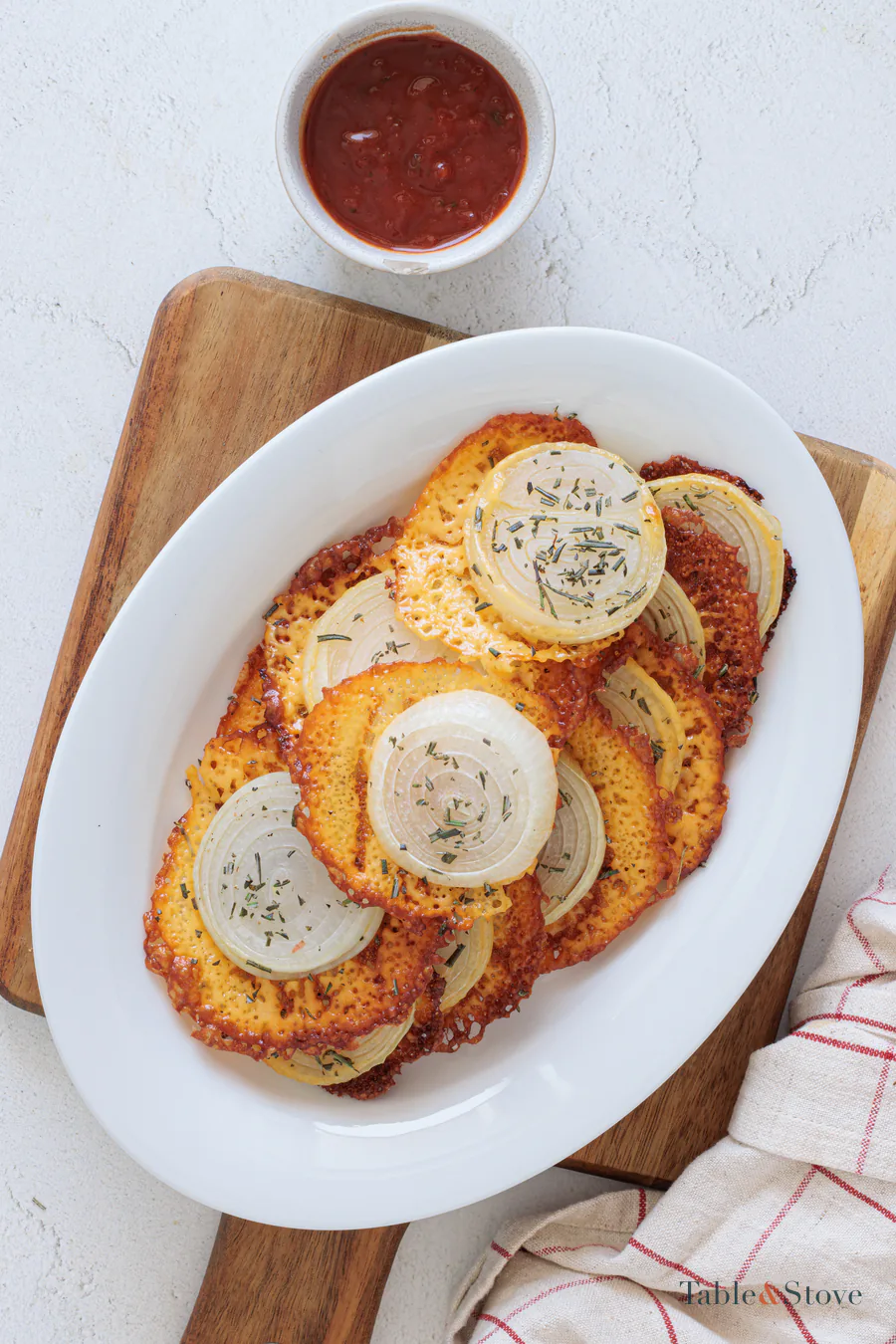 Golden cheddar and sweet onion crisps arranged on a white platter with marinara sauce