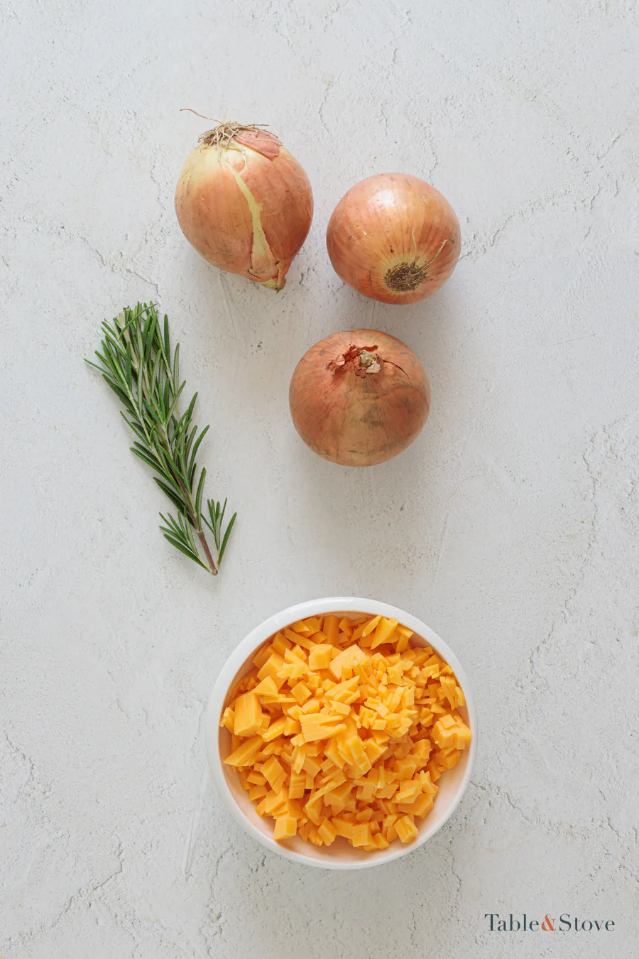Sweet onions, shredded cheddar, and rosemary arranged on a pale surface