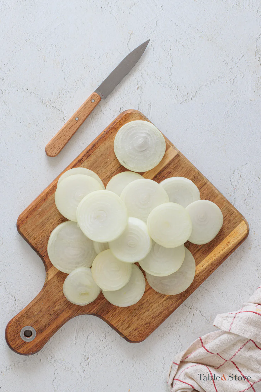 Thin sweet onion rounds separated on a wooden cutting board