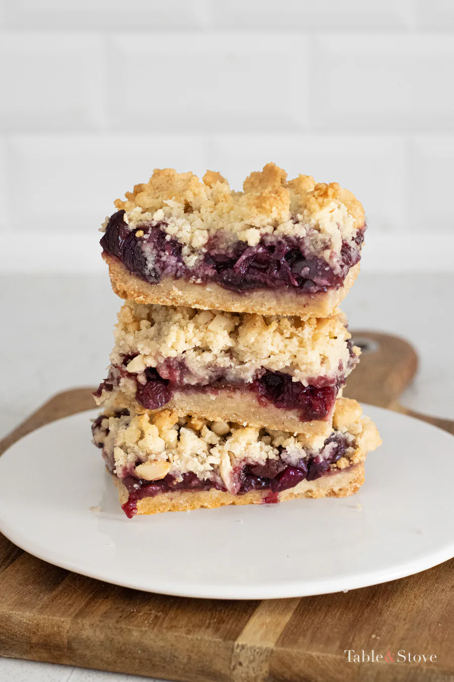 Three cherry pie bars stacked on a white plate, showing the fruit filling and golden crumble