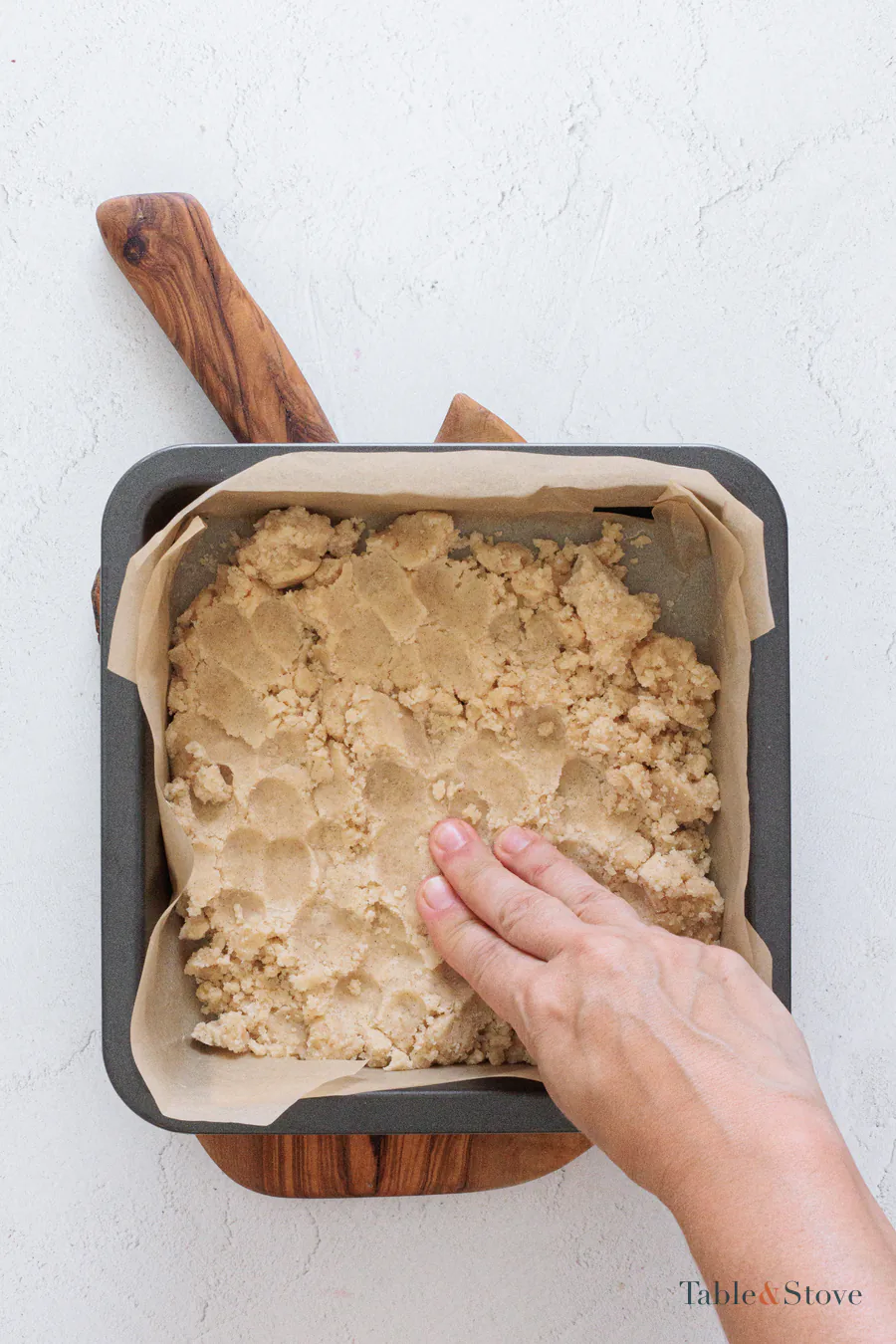 Cherry pie bar dough being pressed into a parchment-lined square pan
