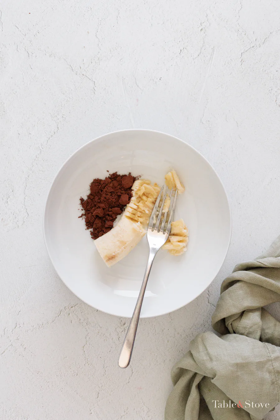 Ripe banana and cocoa powder being mashed together on a plate