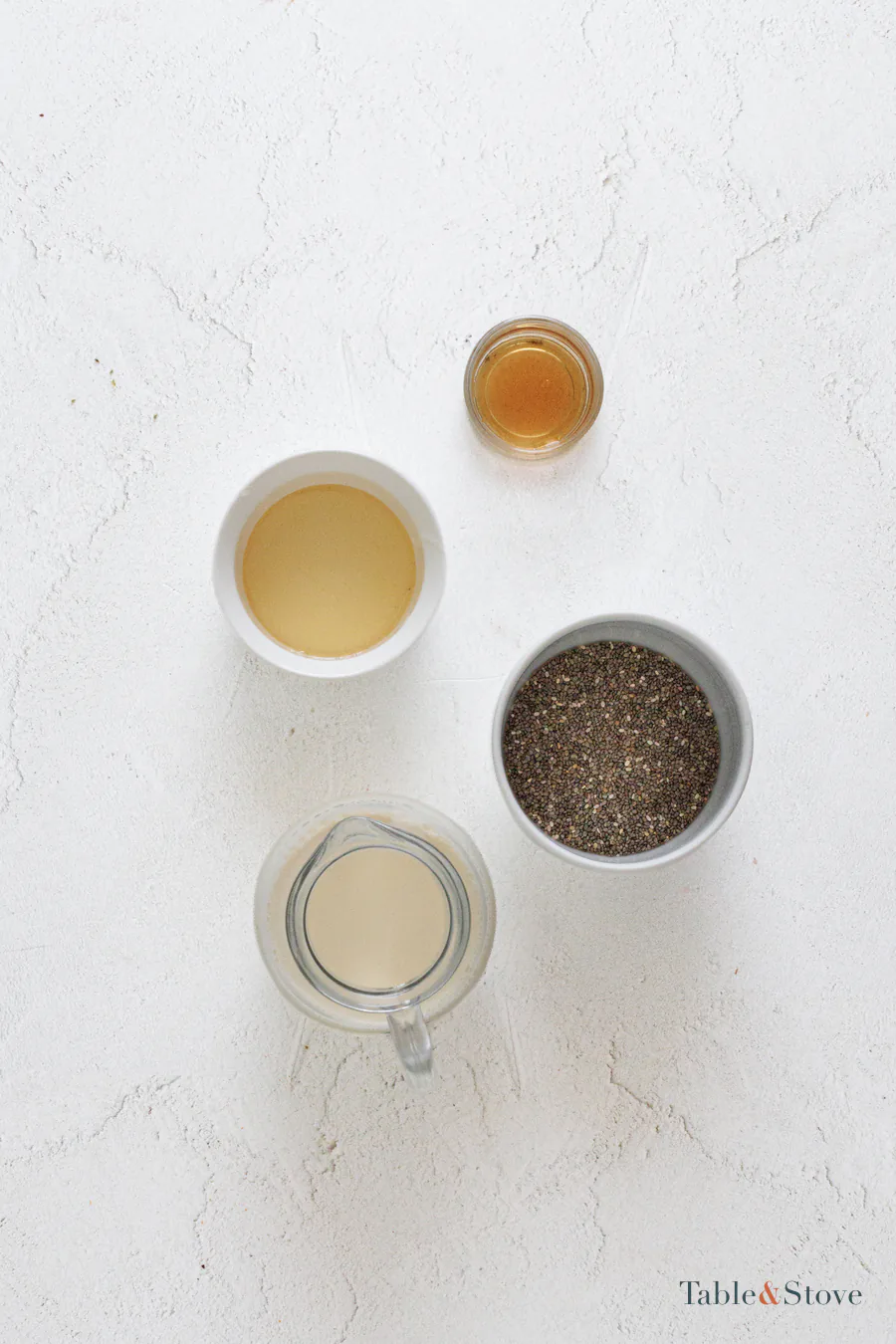 Chia seeds, milk, vanilla, and sweetener arranged on a pale work surface