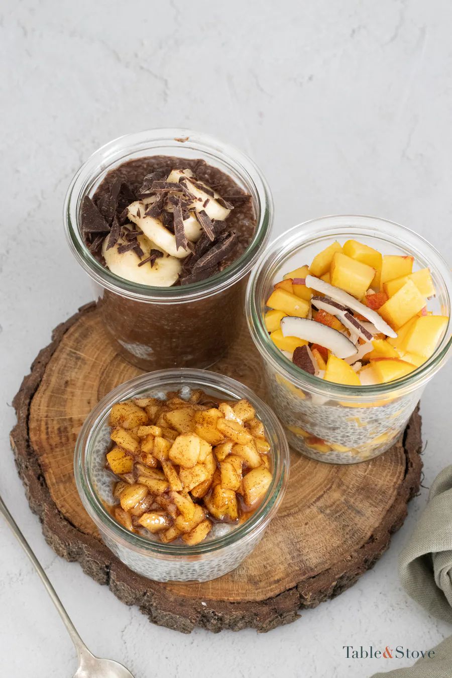 Three jars of chia pudding with banana, peach, and apple toppings