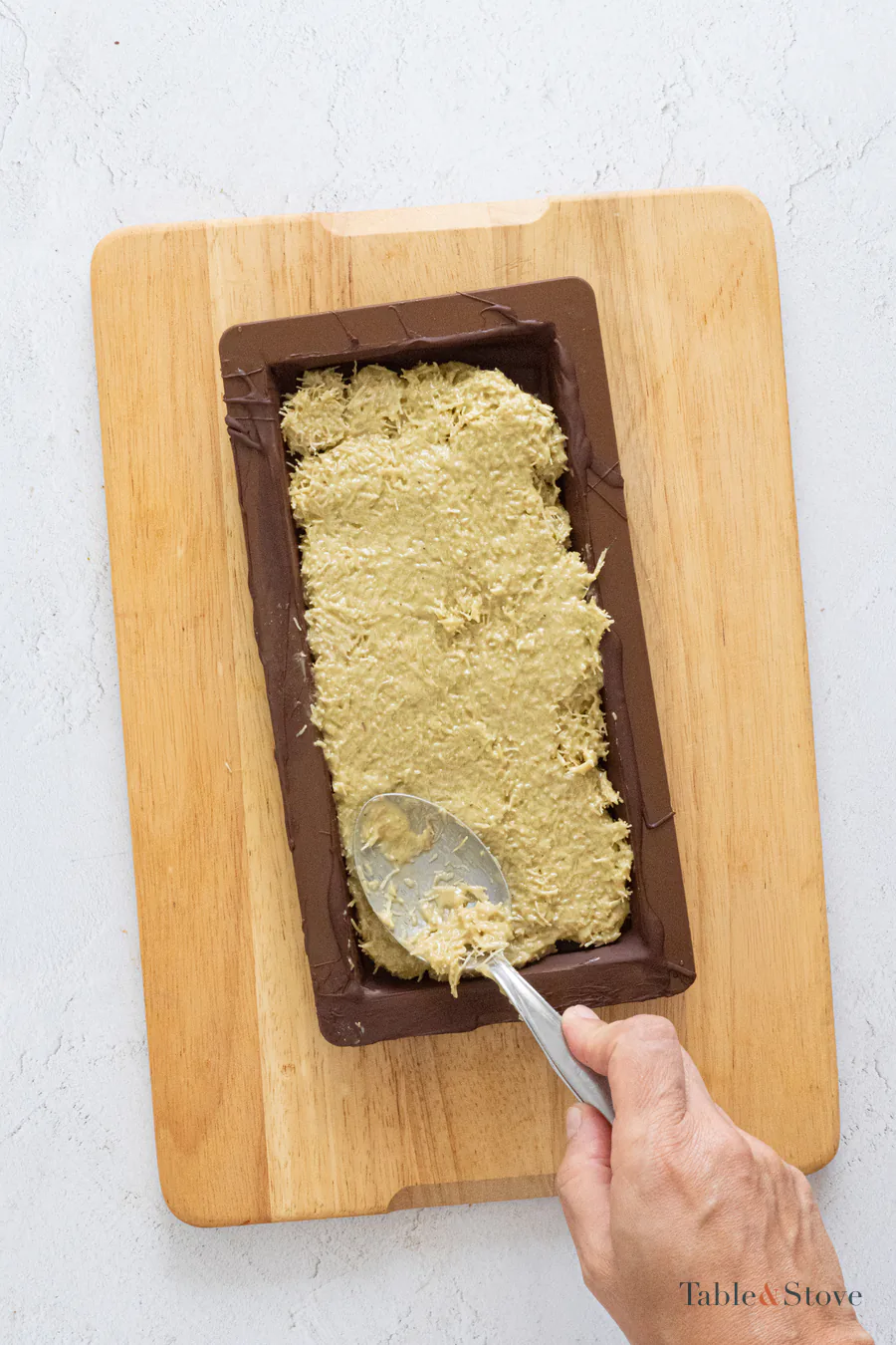 Pistachio kataifi filling being spread inside a dark chocolate shell