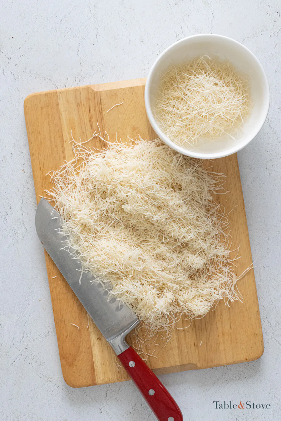 Kataifi pastry being chopped into shorter strands on a wooden board