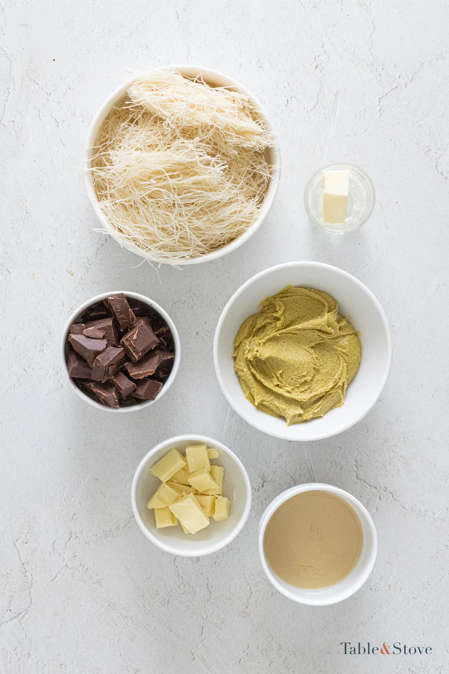 Kataifi, butter, pistachio cream, tahini, white chocolate, and dark chocolate arranged in bowls