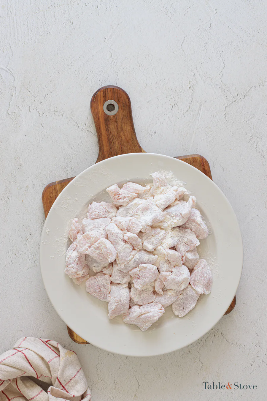 Raw chicken pieces evenly coated with flour in a shallow bowl