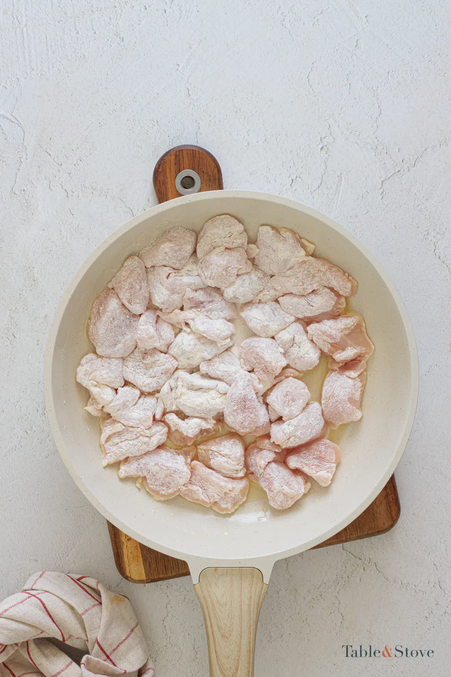 Floured chicken pieces cooking in a single layer in a skillet