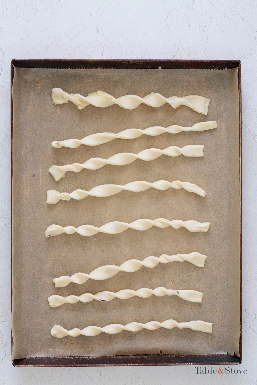 Unbaked puff pastry strips twisted into spirals on a lined baking sheet
