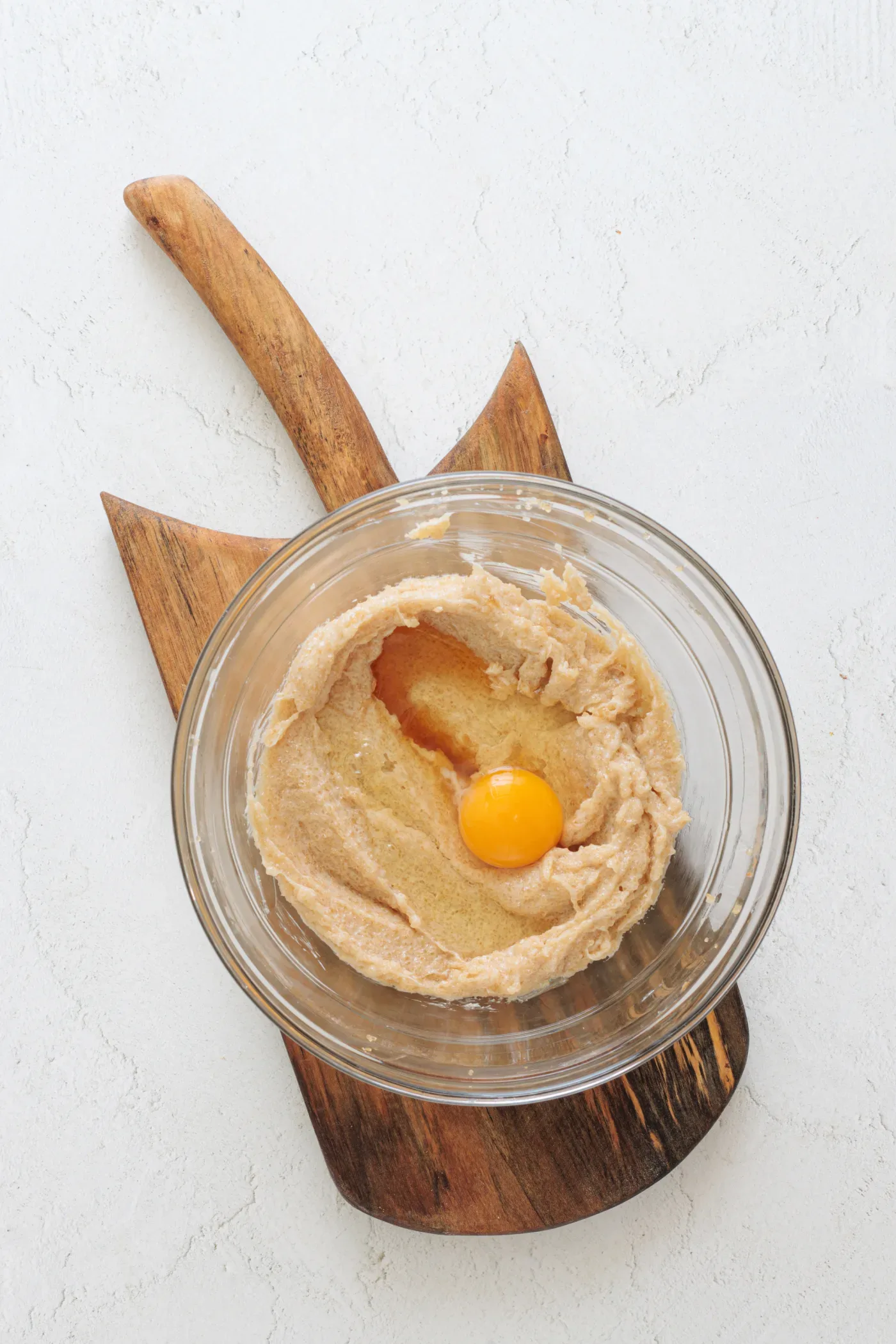 Egg added to the smooth honey cookie mixture in a glass bowl