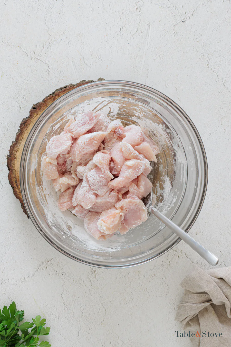Raw chicken pieces coated with cornstarch and salt in a glass bowl