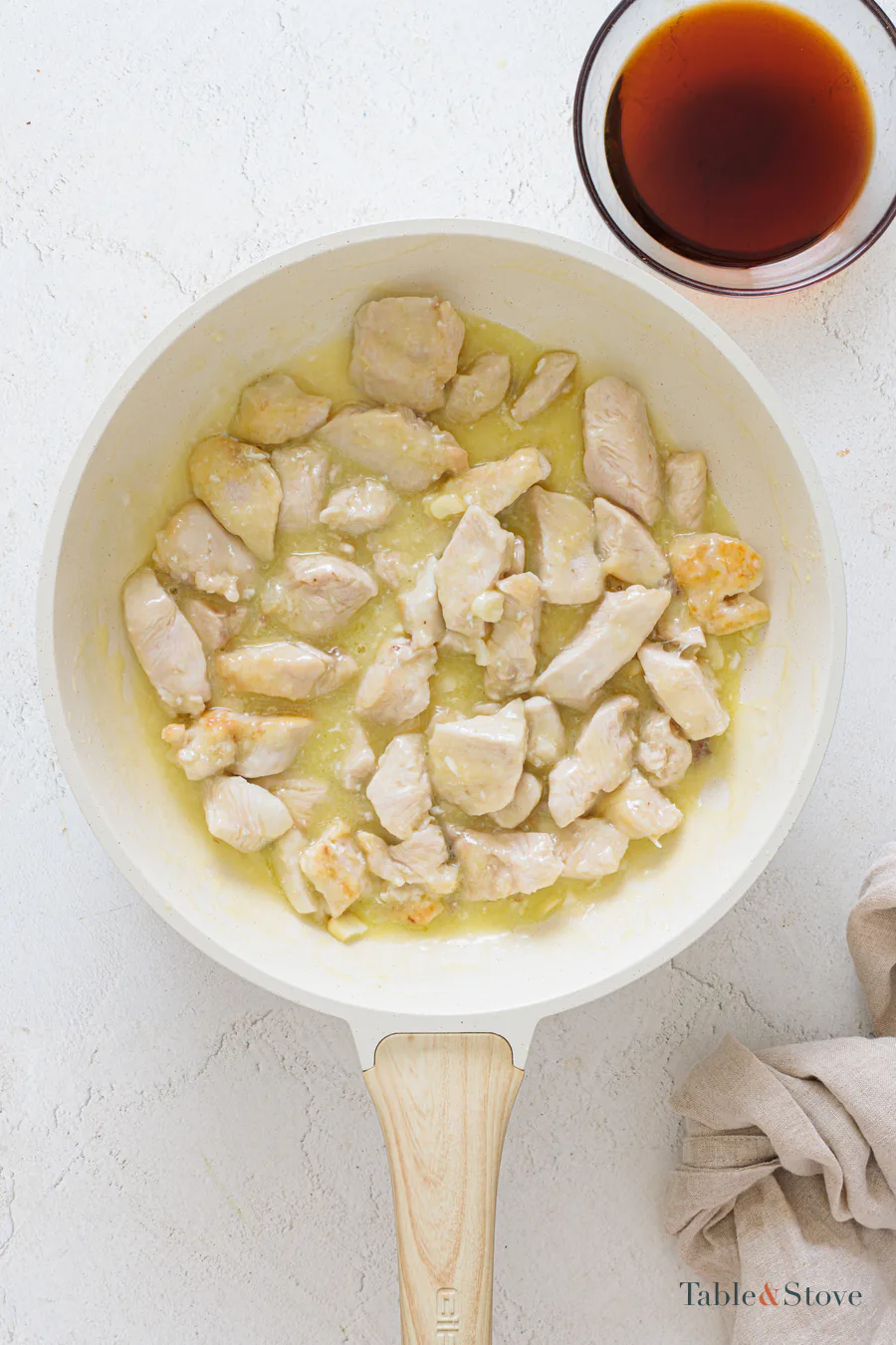Chicken cooking in a skillet beside a small bowl of dark honey soy glaze