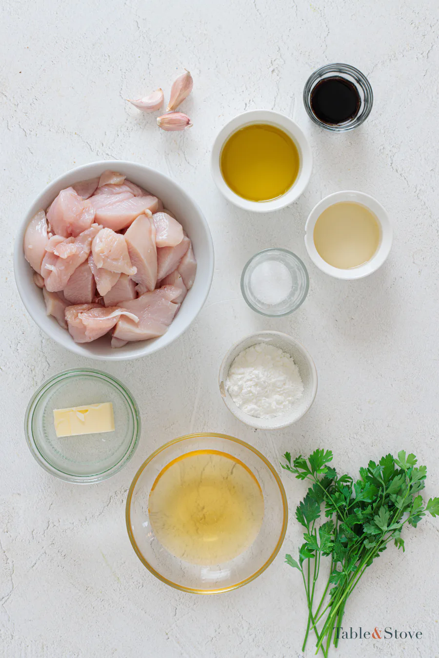 Chicken, cornstarch, honey, soy sauce, vinegar, garlic, butter, oil, and parsley arranged on a pale surface