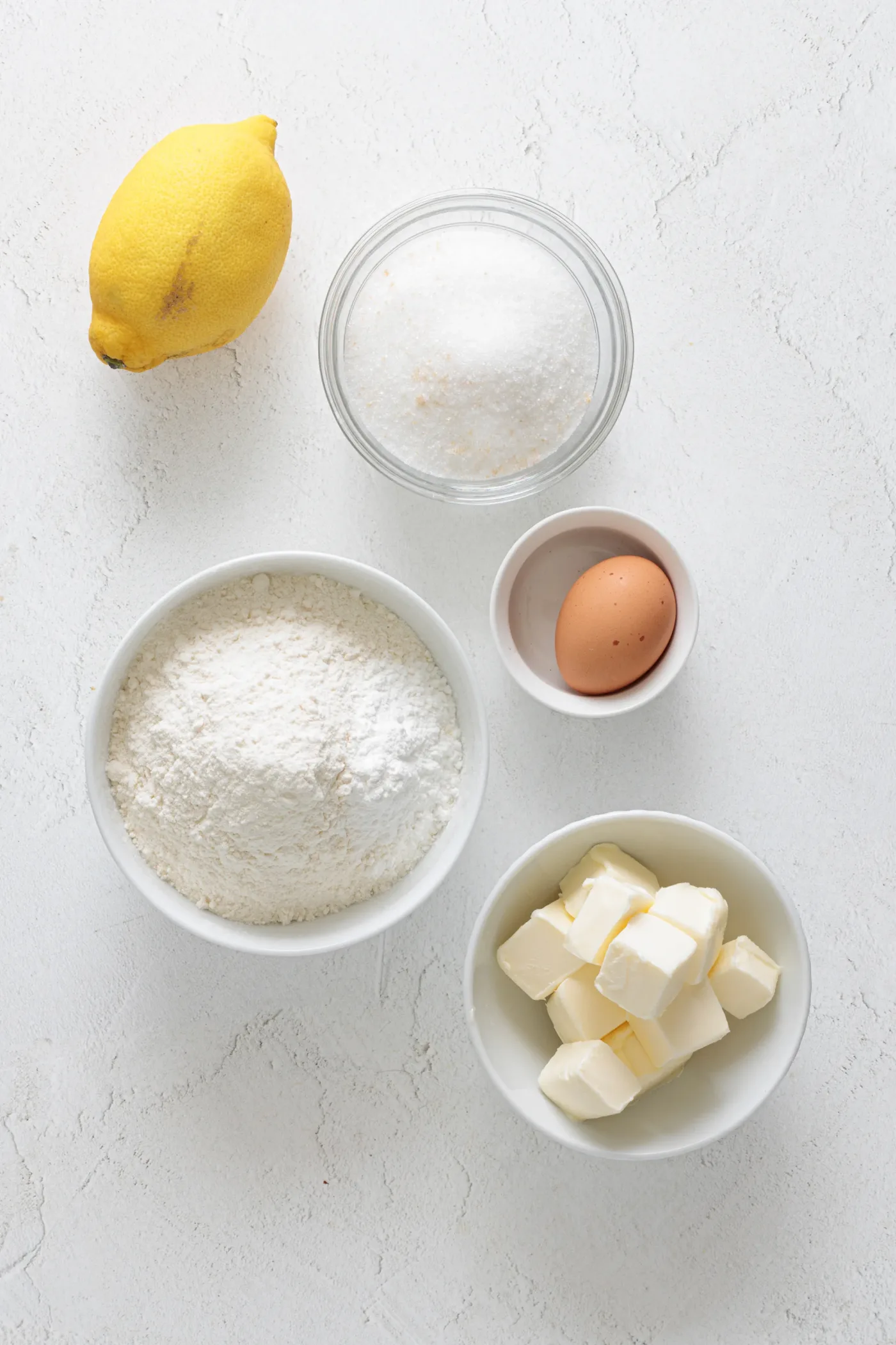 Measured ingredients for lemon crinkle cookies with lemon, flour, sugar, egg, and butter