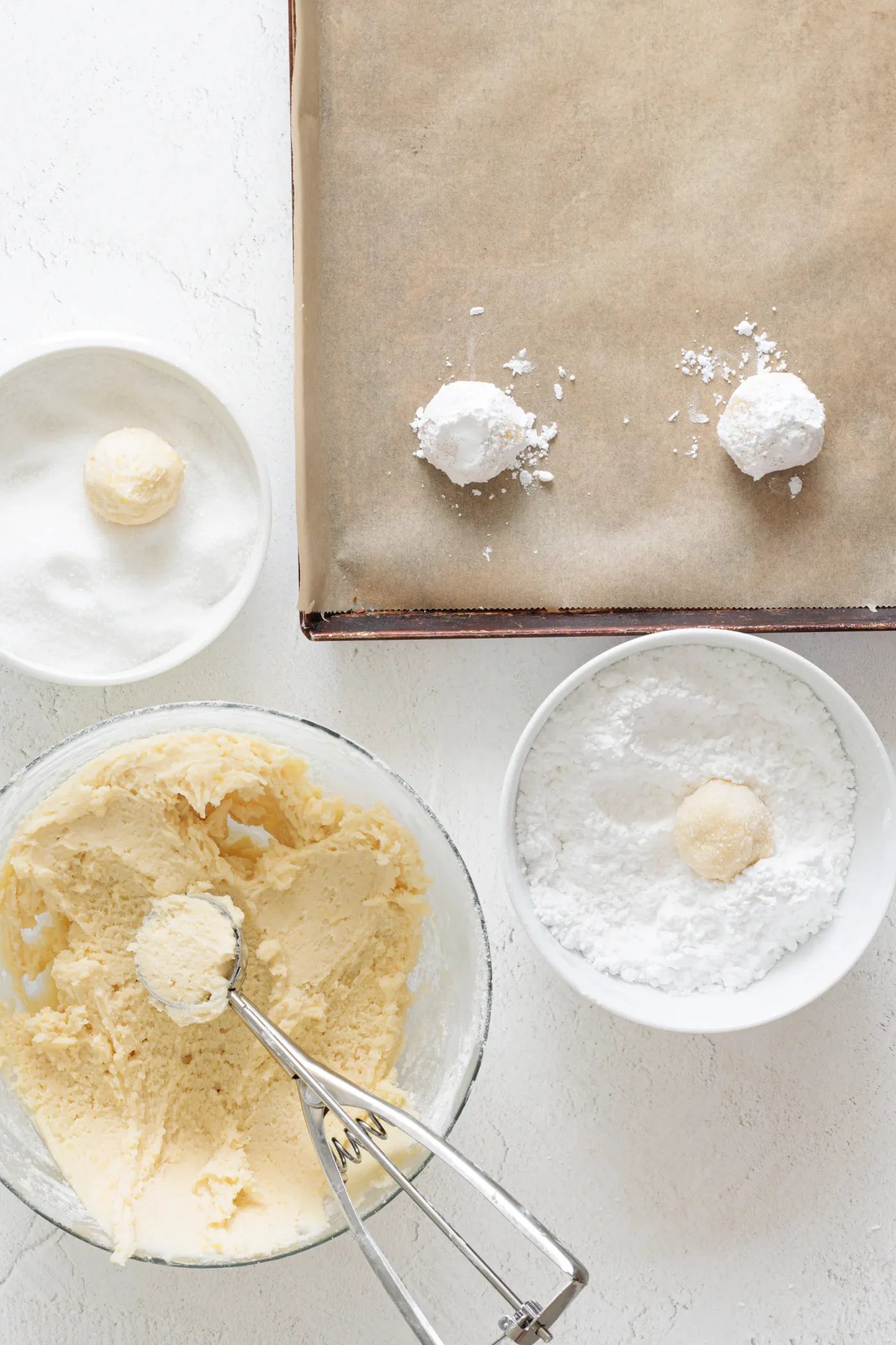 Lemon cookie dough balls rolled in powdered sugar beside a lined baking sheet
