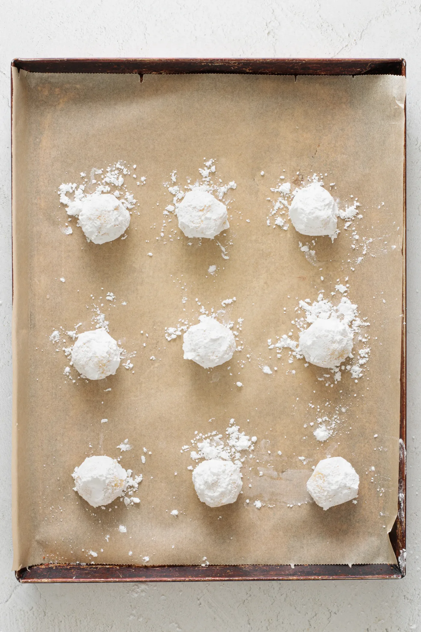 Powdered sugar coated lemon cookie dough balls spaced on a parchment-lined baking sheet