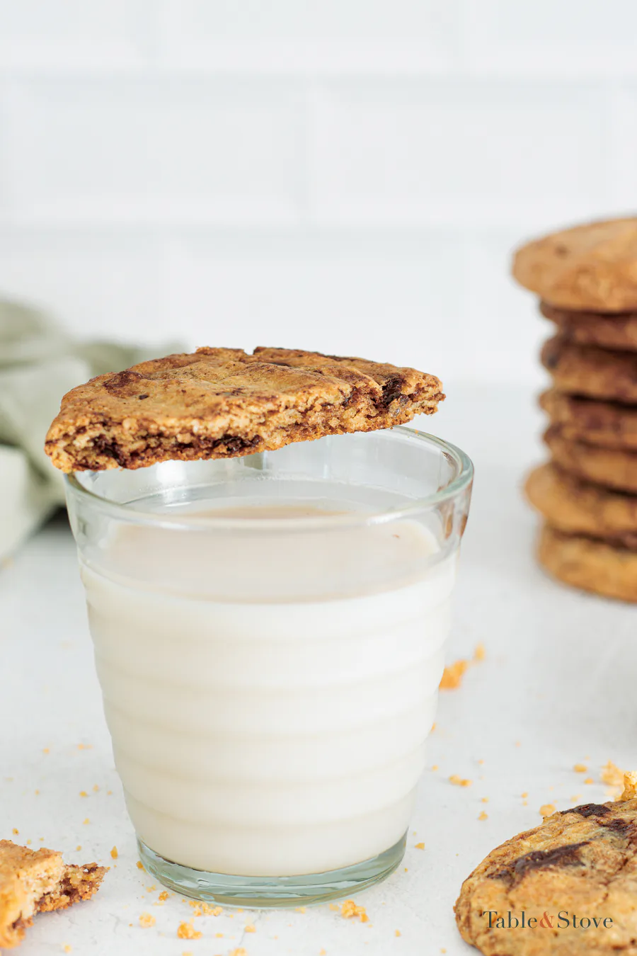 Half of an oat cookie resting on the rim of a glass of milk