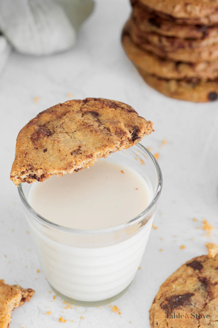 Bitten oat cookie balanced on a glass of milk with more cookies behind it