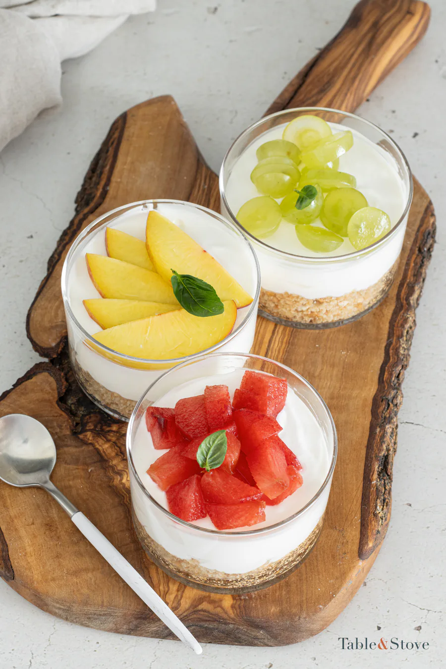 Three mini cheesecake cups topped with different fresh fruits and basil