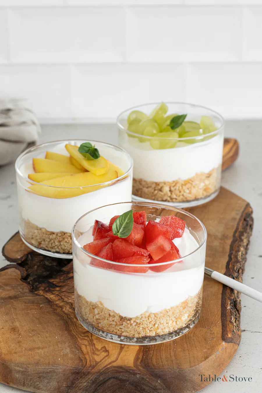 Three chilled cheesecake cups topped with peach, grapes, plum, and basil