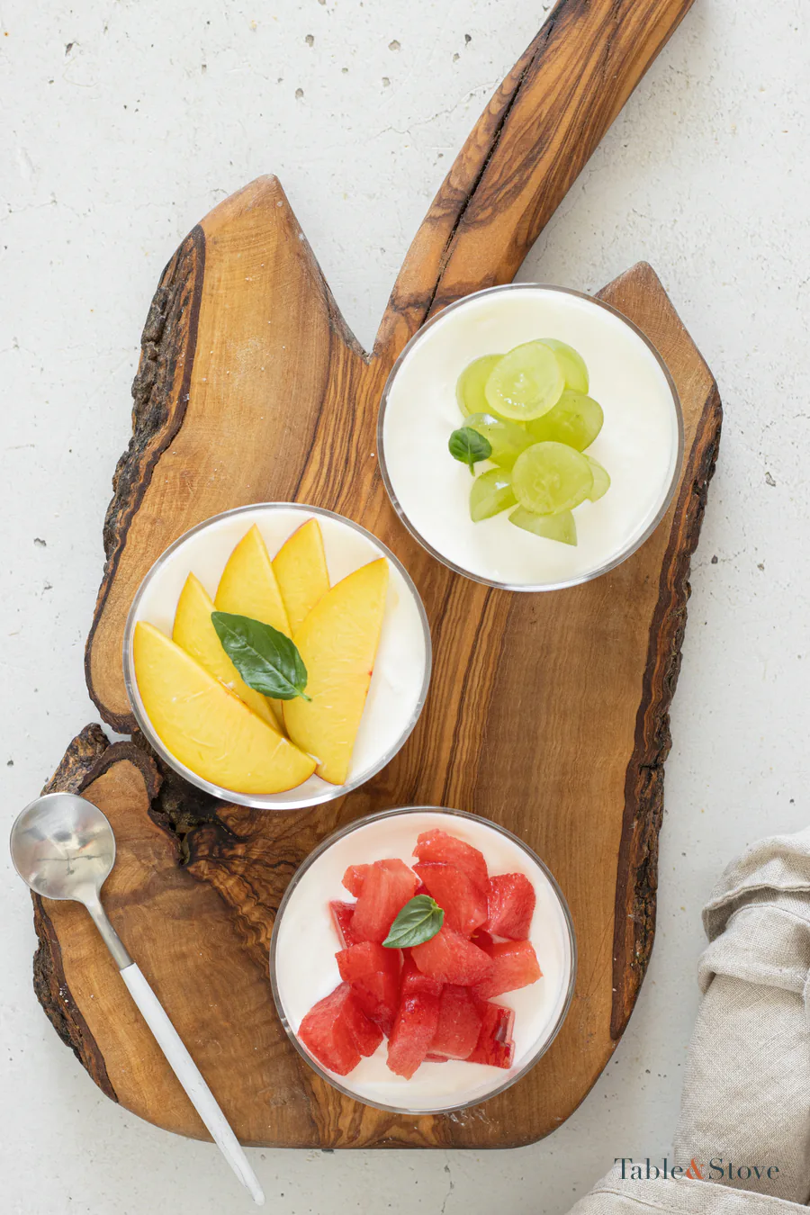 Mini cheesecake cups topped separately with sliced peach, grapes, and plum pieces