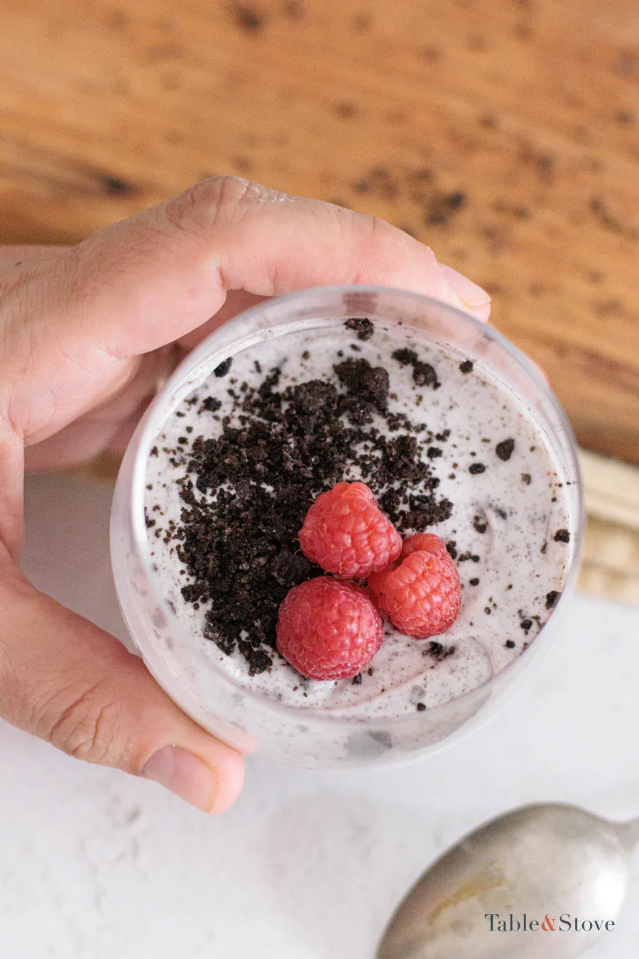 Hand holding a chilled Oreo dessert cup topped with raspberries and crumbs