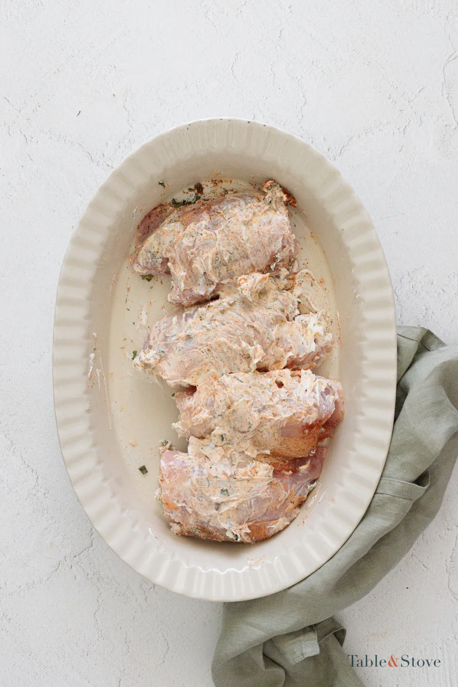 Raw chicken thighs coated with cream cheese and seasonings in a baking dish