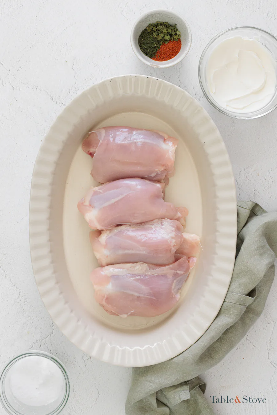 Raw chicken thighs arranged in a white oval baking dish