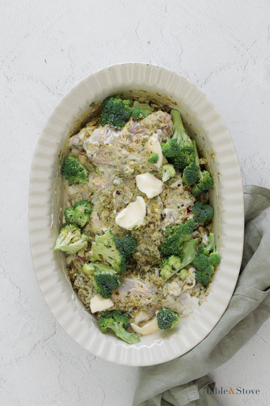 Broccoli florets and butter pieces arranged over creamy chicken in a baking dish