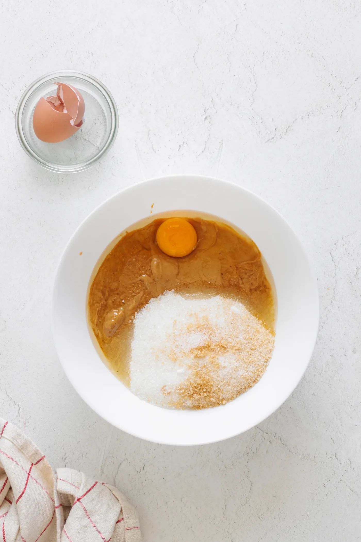 Peanut butter, sugar, and egg in a white mixing bowl