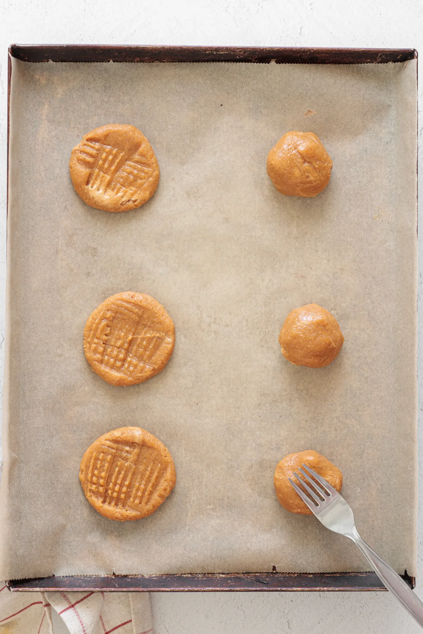 Peanut butter cookie dough portions on a parchment-lined baking sheet, some marked with a fork