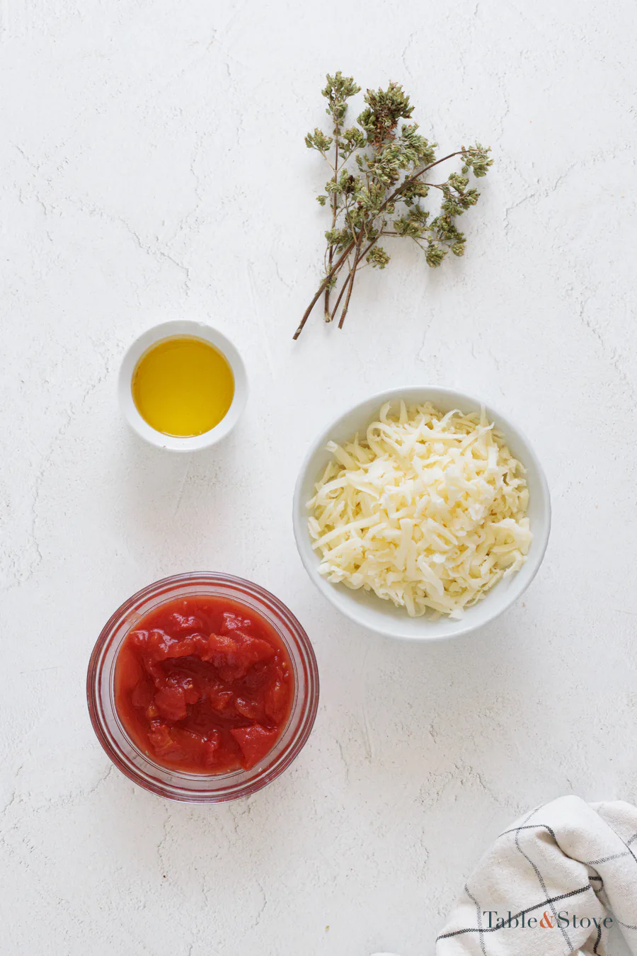 Tomato passata, shredded mozzarella, oregano, and olive oil arranged beside the dough