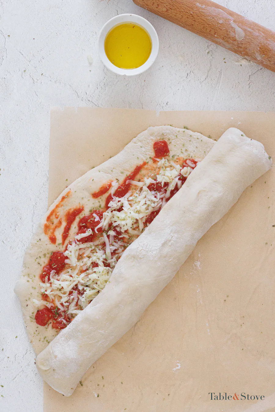 Filled pizza dough being rolled tightly into a log