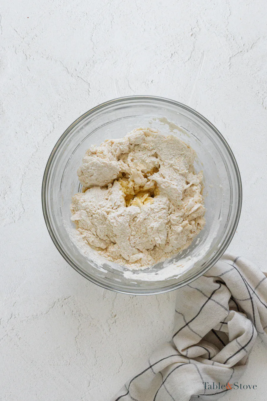 Partially mixed pizza dough with loose flour in a glass bowl