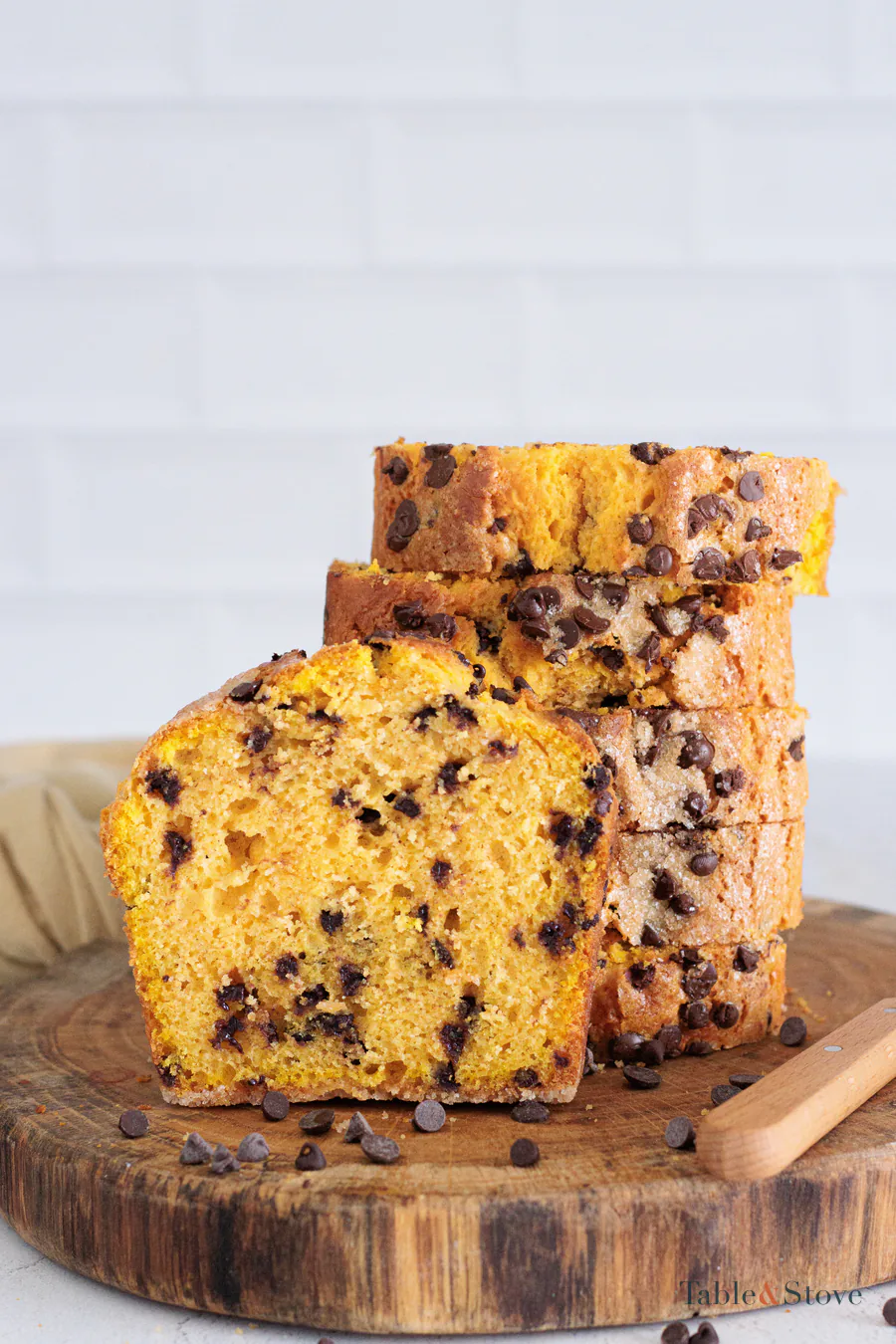 Sliced pumpkin bread with chocolate chips in the orange crumb and a loaf behind it