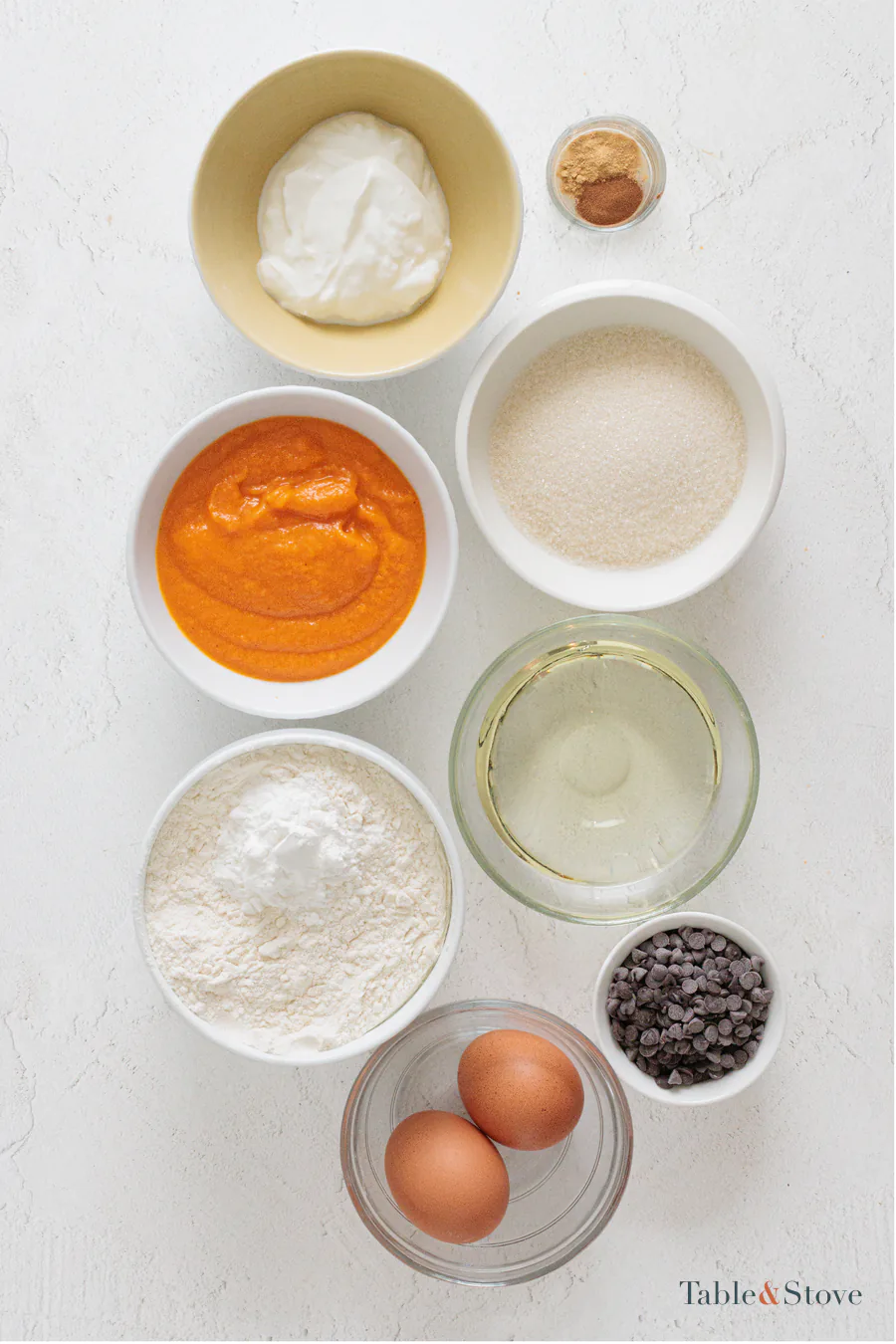 Eggs, sugar, pumpkin puree, oil, soy yogurt, flour, cinnamon, baking powder, and chocolate chips set out for pumpkin bread