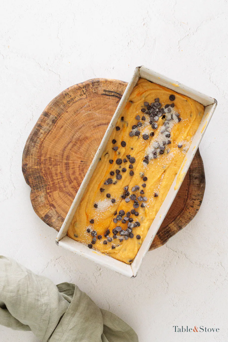 Pumpkin bread batter in a lined loaf pan, with decorative chocolate chips and sugar visible on top
