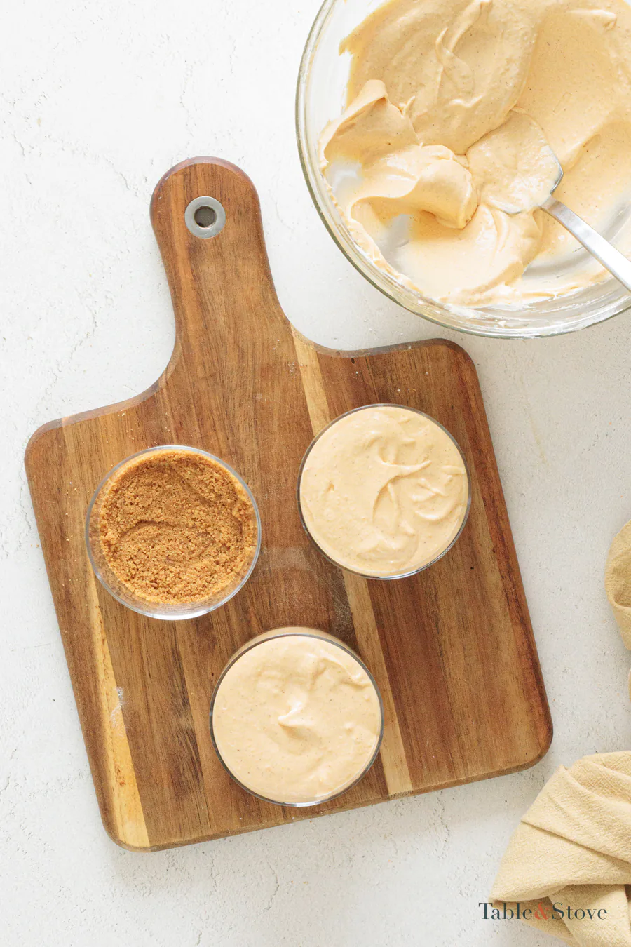 Pumpkin cheesecake filling being added to clear glasses over cookie bases