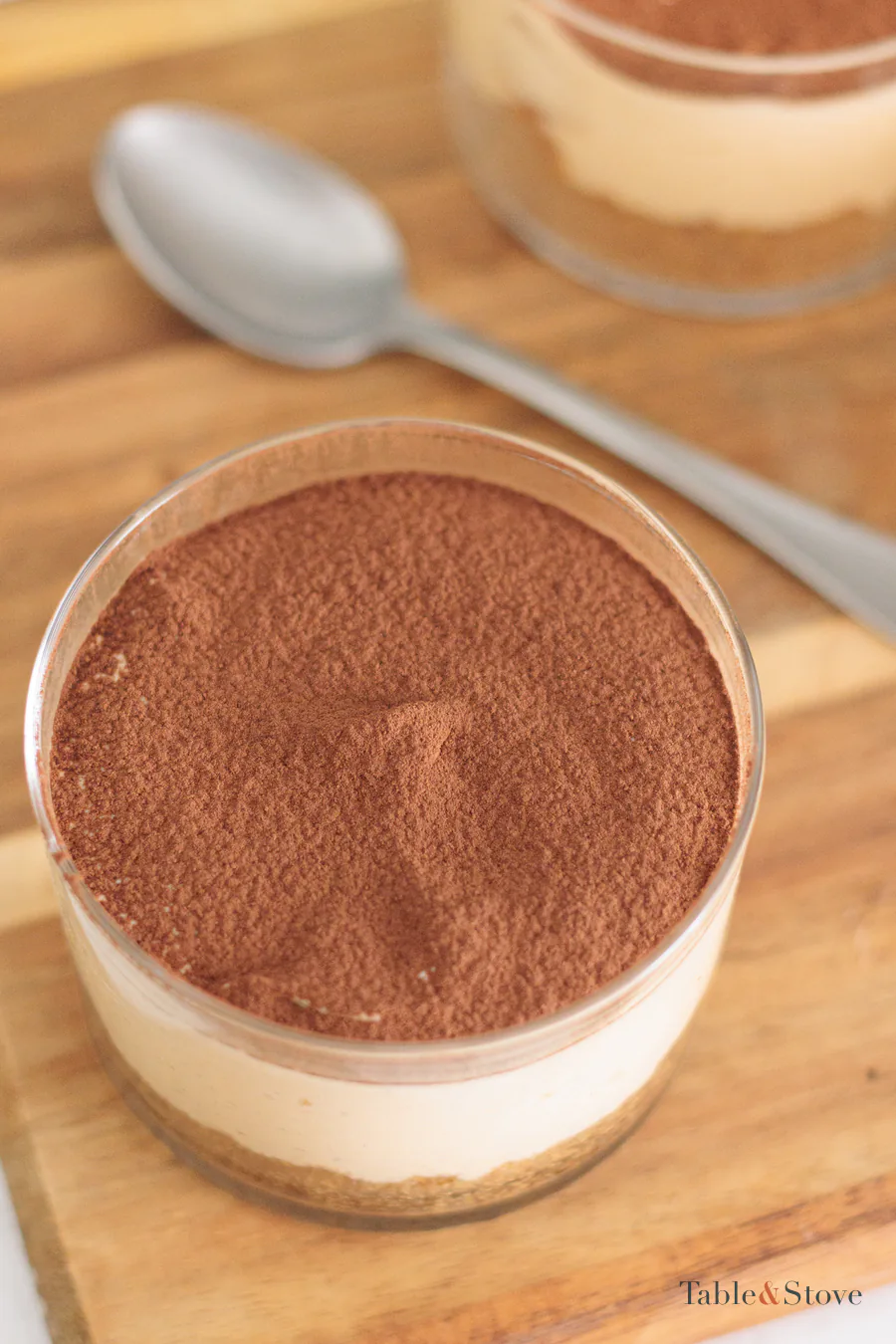 A glass of pale orange pumpkin cheesecake with a cookie base and cocoa dusted over the top