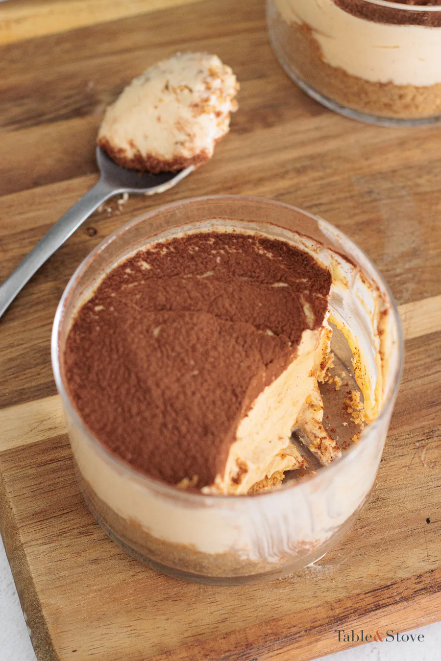 A spoonful taken from a pumpkin cheesecake cup, revealing the filling and cookie base